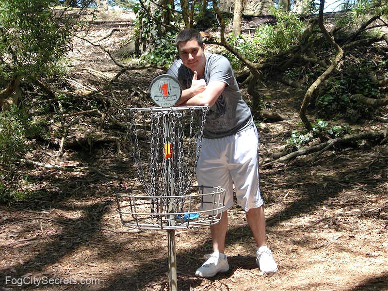 Man leaning on first hole basket on SF disc golf course Man leaning on first hole basket on SF disc golf course