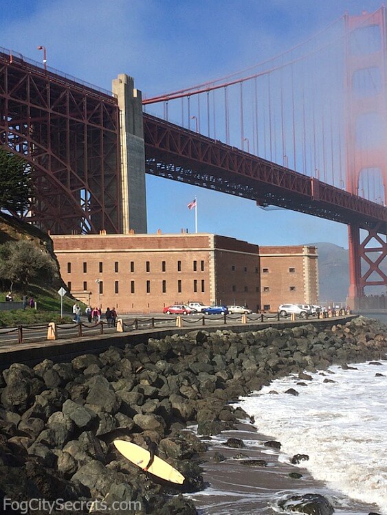 Fort Point under the Golden Gate Bridge, with surfer climbing the rocks.