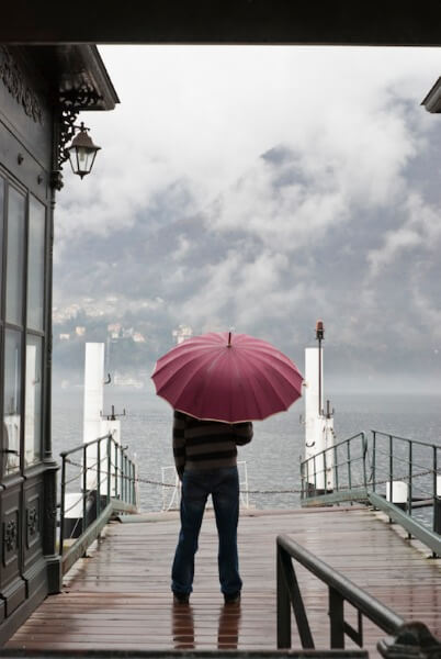 Man on stormy dock with umbrella.